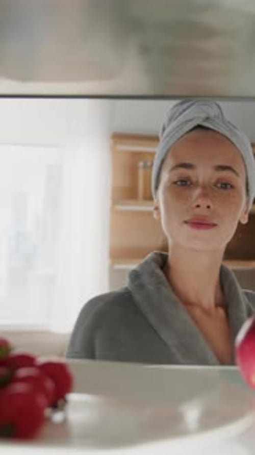 Woman in bathrobe takes an apple from refrigerator