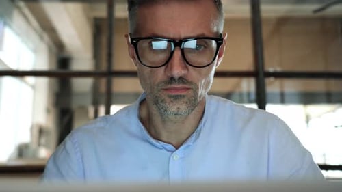 Man wearing glasses looking at computer screen indoors