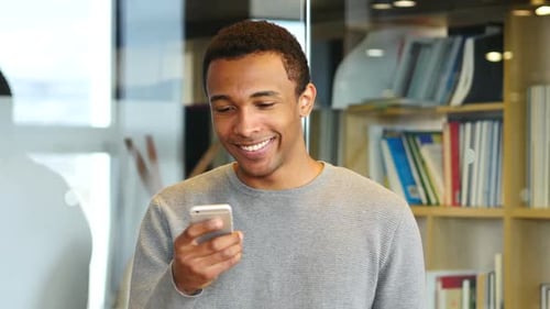 Man Using Smartphone and Smiling Indoors