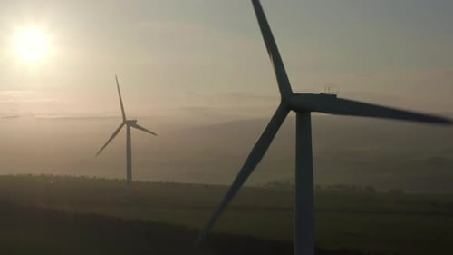 An aerial view of two windfarm turbines slowly turning with the evening sun behind them, Aberdeensir