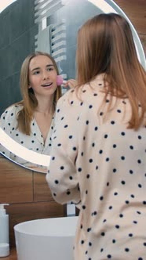 Happy Woman Massaging Face in Bathroom Mirror