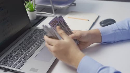 Hands Counting Money Near Laptop in Office