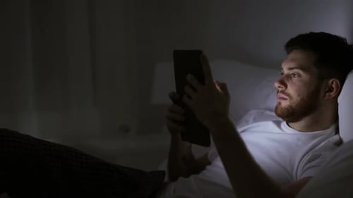 Man Uses Tablet Lying in Bed at Night
