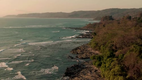 Aerial tilt reveal shot of breaking waves on rocky Costa Rica jungle coastline