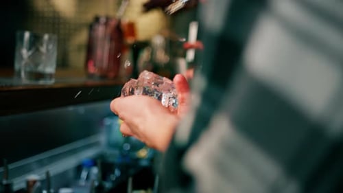 The bartender breaks the ice Close-up of male hands cracking ice with a sharp tool in a bar