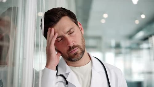 Tired Doctor Leans Against Wall in Hospital Close Up