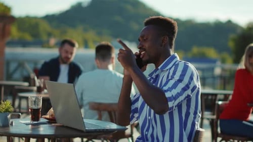 Close Up Handsome African American Young Man in Sitting at the Table with Laptop Talking on Phone