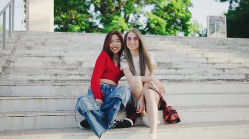 Two Beautiful Girls are Sitting on the Steps in the Park Portrait of Young Beautiful Women