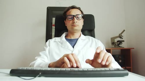 Slow Motion a Man in a White Coat and Glasses Works Intently on a Computer Scientific Activity of a