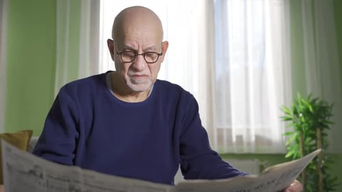 Senior Man Reads Newspaper Inside Home