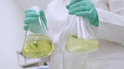 Chemiker in Laborkittel und Gummihandschuhen schüttelt gelbe Proben vor der Analyse kräftig