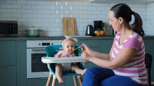 Mother feeding baby in high chair in the kitchen