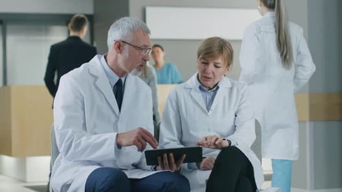 In the of the Hospital Two Professional Doctor Have Discussion, Using Tablet Computer, while Sittin