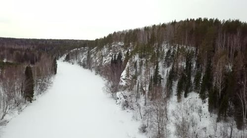 A Serene Winter Landscape Showcasing a Snow Covered River Alongside a Beautiful Forest Stock Clip