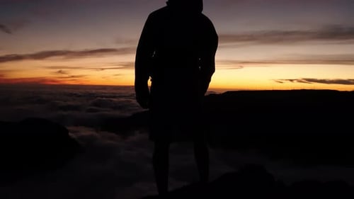 A man stands still at Pico do Arieiro in Madeira, silhouetted against a glowing sunset sky and sea o