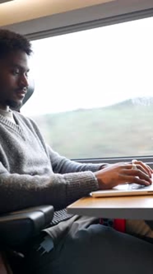 Schwarzer männlicher Freelancer, der während einer Geschäftszugreise aus der Ferne am Laptop arbeitet