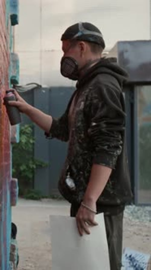 Male Artist in Respirator Creating Mural on Wall in Street