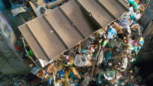 An excavator loading garbage onto a conveyor belt at waste sorting plant. Slow motion