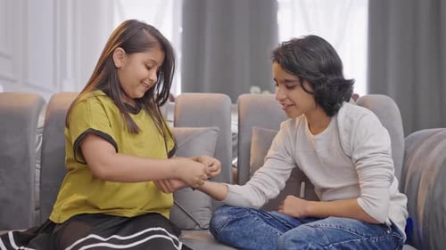 Girl Ties Bracelet on Brother's Wrist on Couch