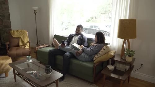 Couple Relaxing on Couch Reading and Using Phone