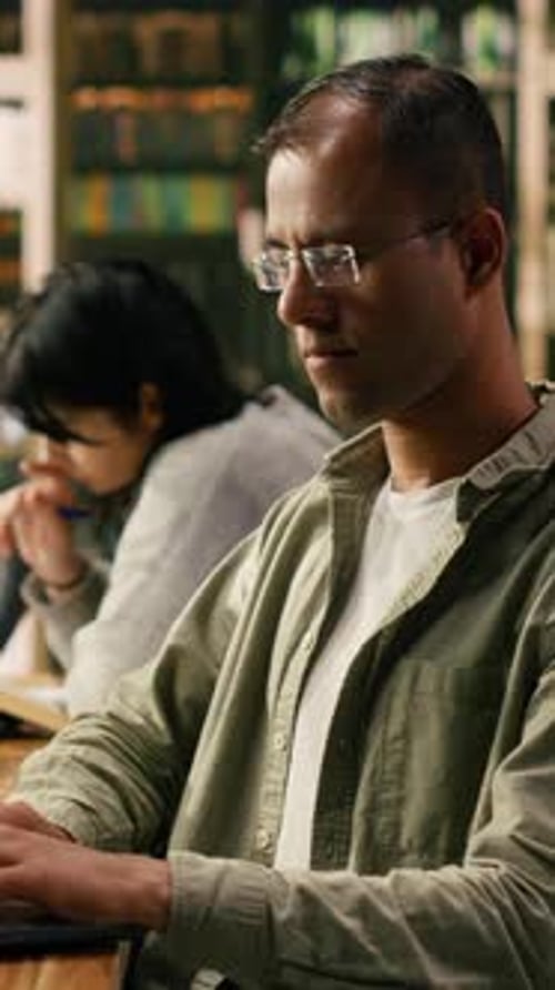 Vertical Video Adult Man Concentrating on Note Taking on Laptop at Wooden Library Desk