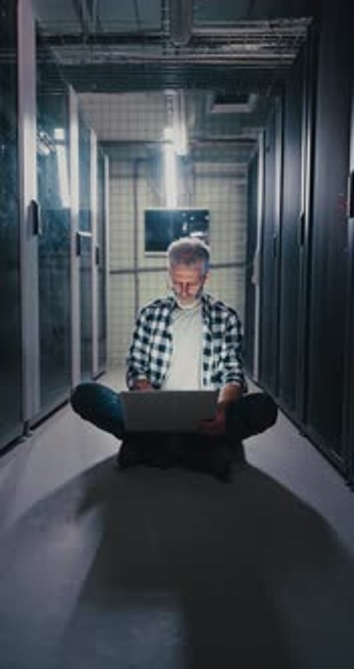Man Working on Laptop in Data Center Hallway