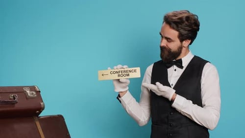 Bellhop Points to Conference Room Sign with Luggage
