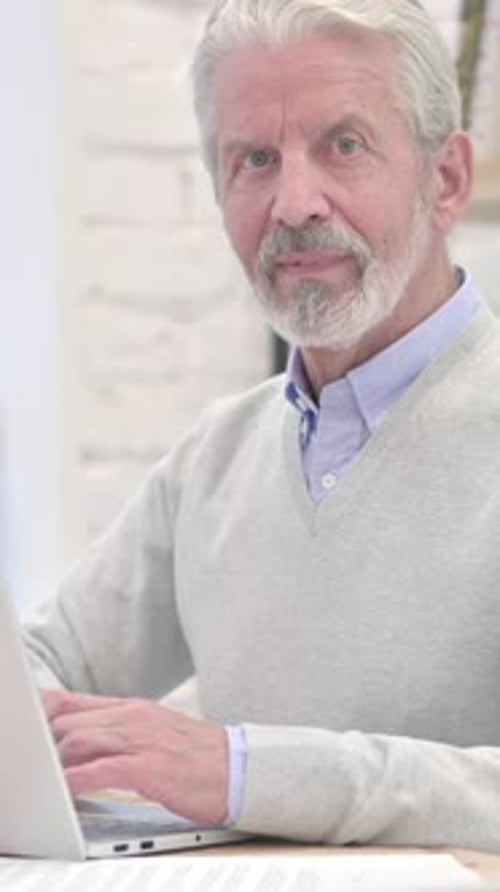 Senior Man Working on Laptop, Looking at Camera