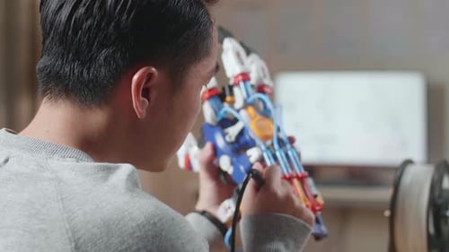Over The Shoulder View Of A Male With 3D Printing Repairing A Cyborg Hand At Home
