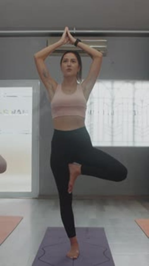 Woman Practices Tree Pose in Yoga Studio