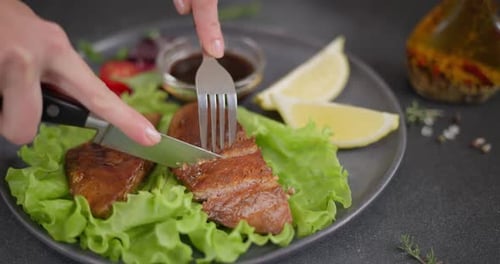 Woman Slicing Fried Grilled Piece of Organic Tuna Steak on a Black Ceramic Plate with Salad