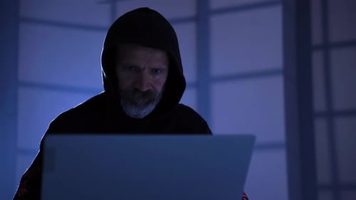 Male hacker working on computer in a dark office room.