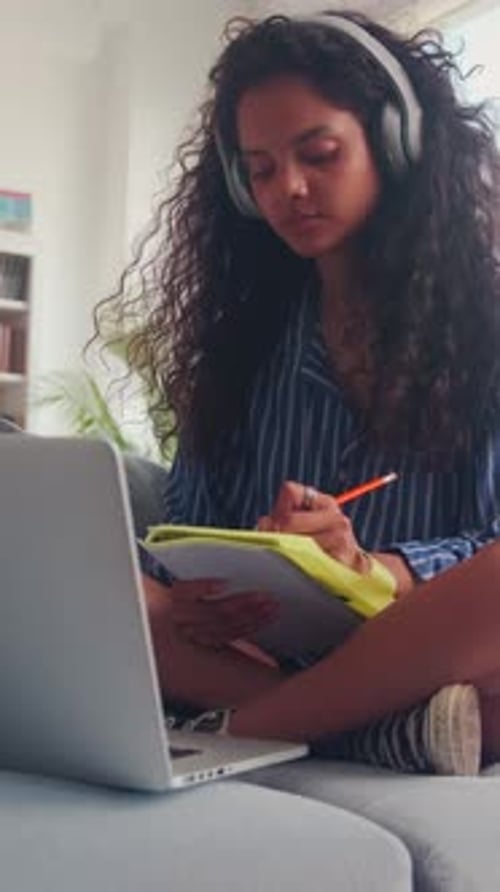 Young Indian Woman Watching Lecture on Laptop and Making Notes in Workbook