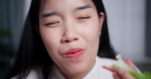 Young Asian woman sitting at a dining table eating salad rolls