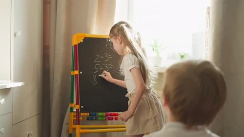 Girl Writes Math Problems for Brother Playing School at Home