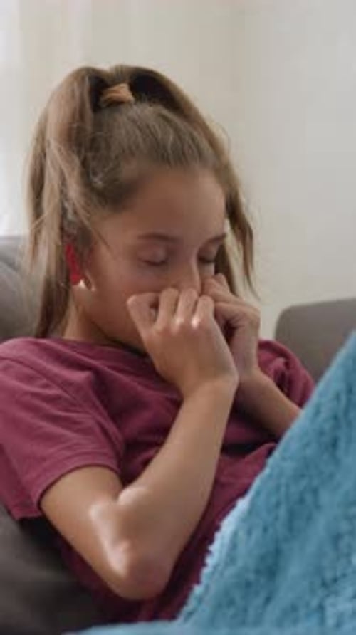 Fille couverte d'une couverture éternuant sur le canapé