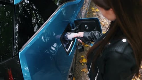 Woman charging her electric car and waits when vehicle will charged at green forest. Save ecology al