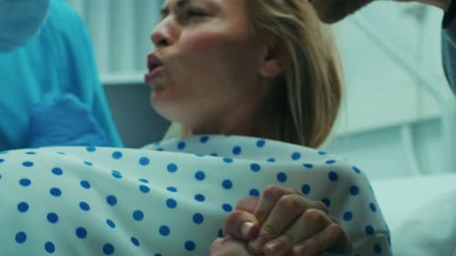 Primer plano del rostro de una mujer en trabajo de parto que se esfuerza por dar a luz, con la ayuda de obstetras, su cónyuge