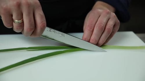 Hands Chopping Green Onions with Knife on Cutting Board