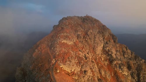 Aerial view of rugged mountain peak during golden hour with hikers exploring summit