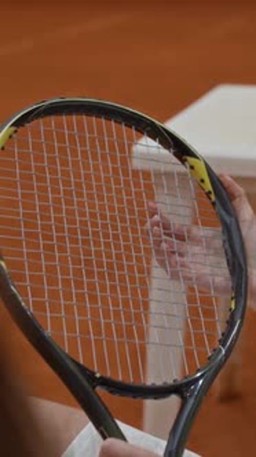Vertical of Woman Checking Strings of Tennis Racket before Match on Clay Court