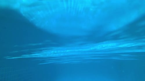 Split footage of just above and beneath the wavy surface of the water in a swimming pool.