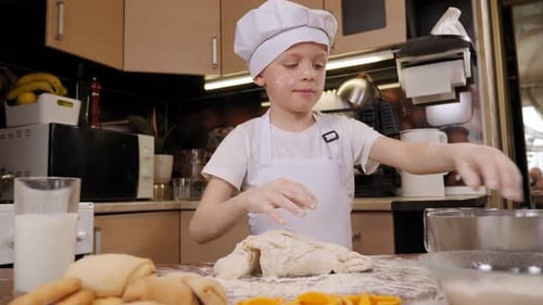 A Boy in an Apron with a Face Stained with Flour Kneads the Dough in the Kitchen