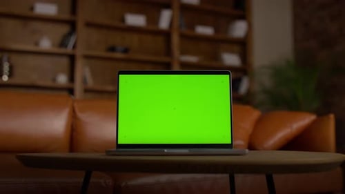 Laptop with Green Screen on Table in Cozy Room