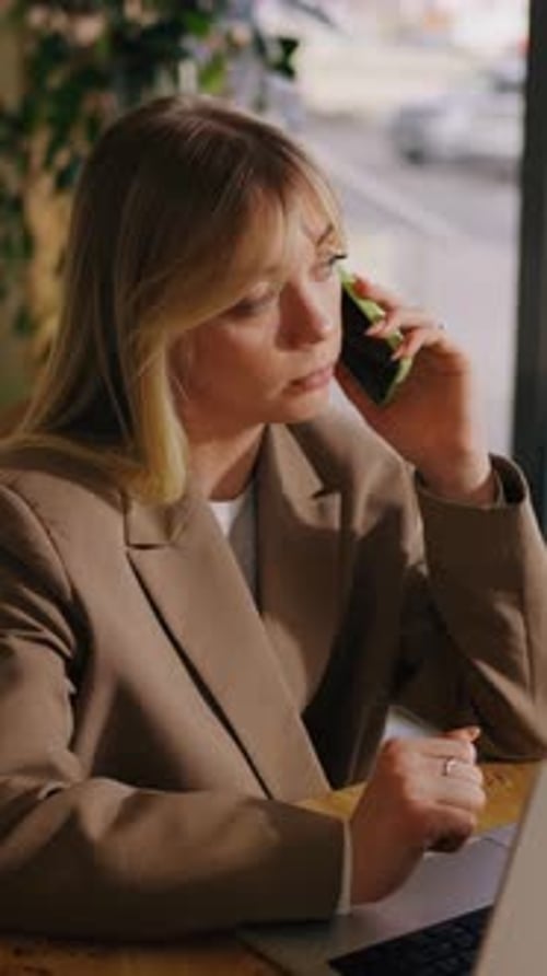 Woman Using Laptop and Talking on Smartphone Indoors
