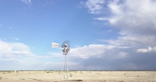 Drone — low angle, slowly moving across the landscape with windmill and skies in background, Texas
