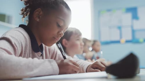 In Elementary School Classroom Black Girl Writes in Exercise Notebook, Taking Test. Junior Classroo