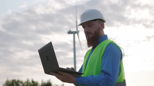 An Engineer Working on His Laptop at a Wind Farm Contributing to Renewable Energy