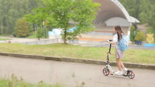 Niña con mochila va a la escuela en patinetaVista trasera