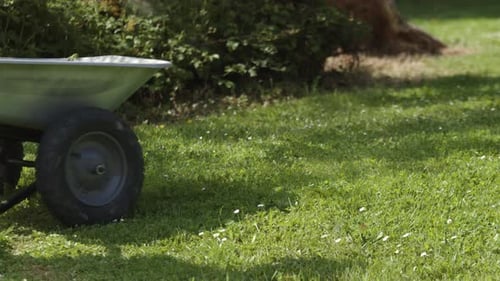 Cropped View Of Farmer Working On The Garden Pushing Wheelbarrow.